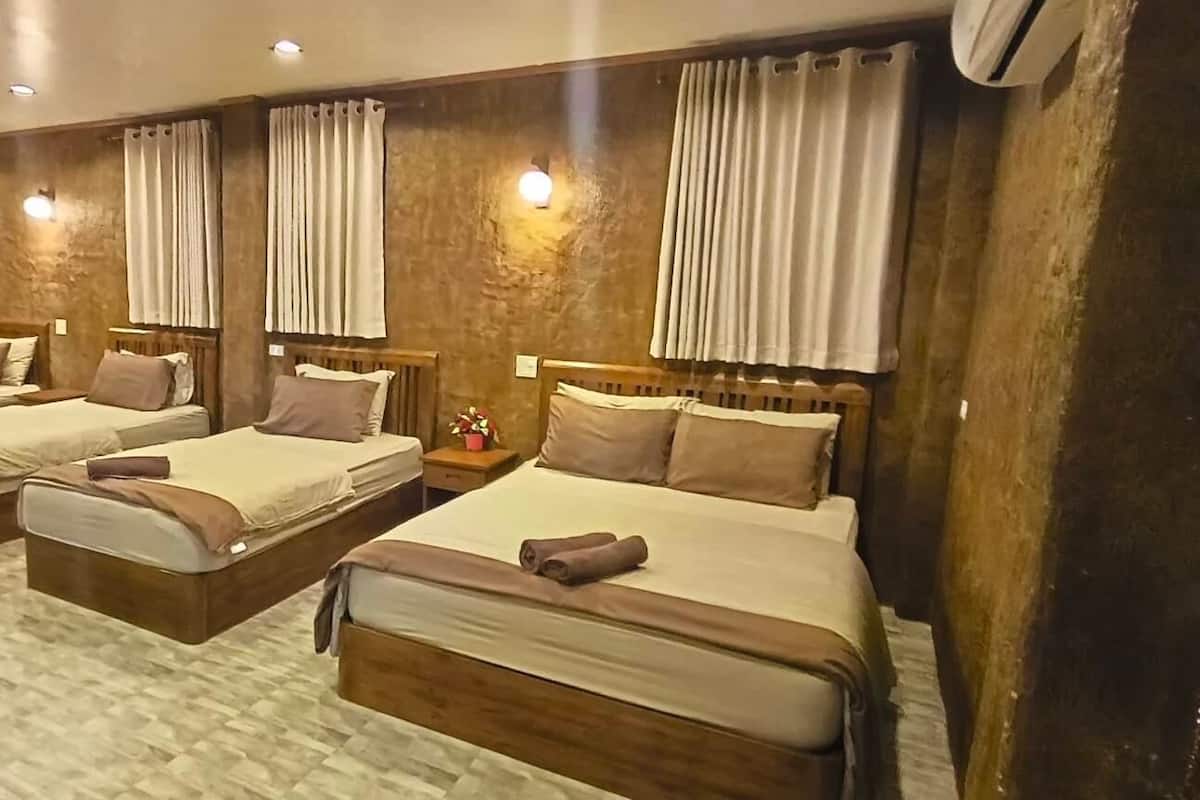 A hotel room with three beds arranged in a row, a large tree trunk decoration, and a textured floor.
