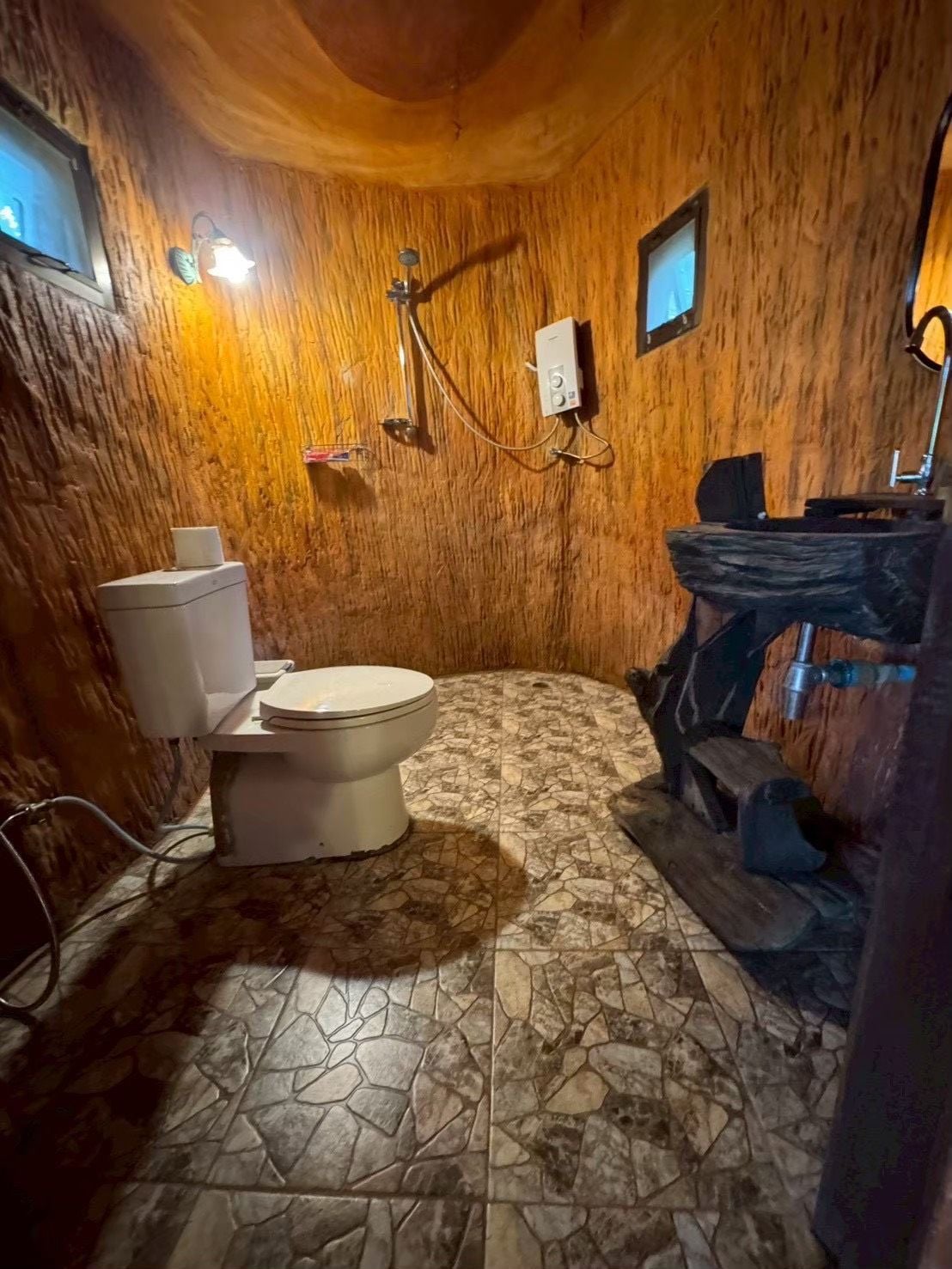 A bathroom with a wooden wall, a toilet, a sink, and a shower area.