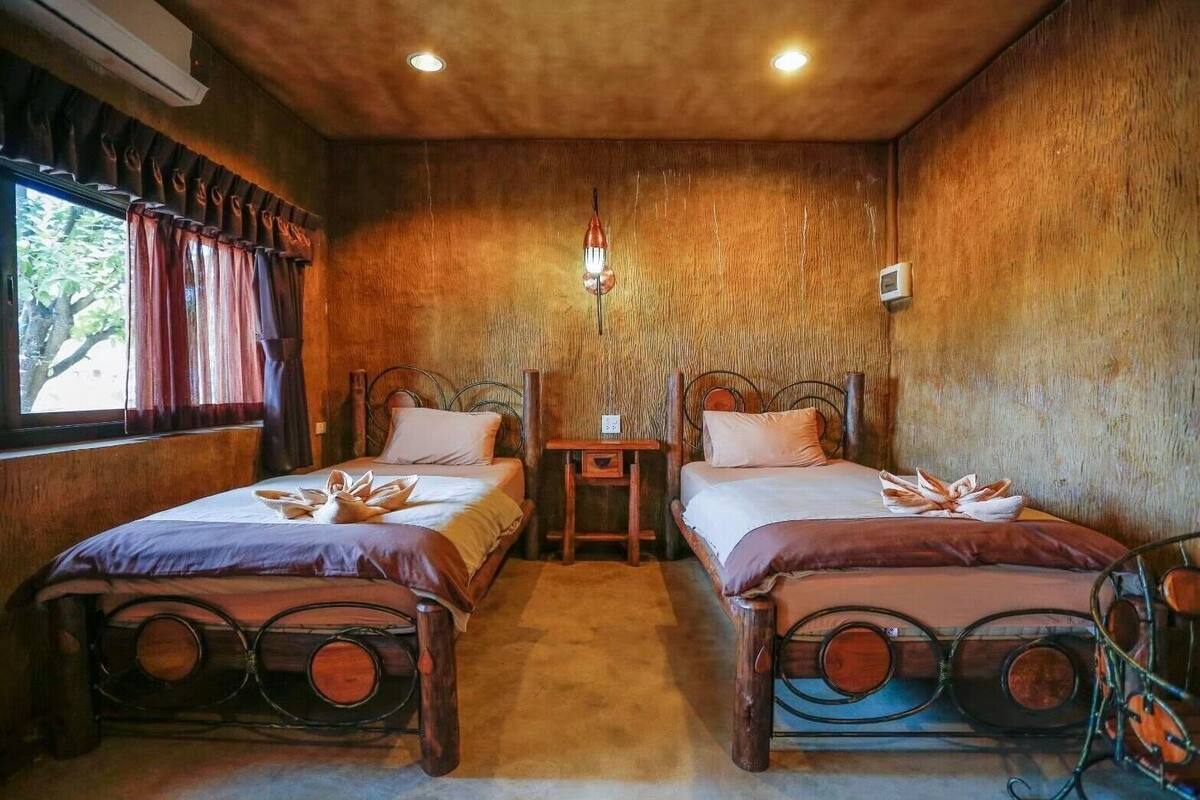 A room with two wooden beds, a small table, and a window with curtains.