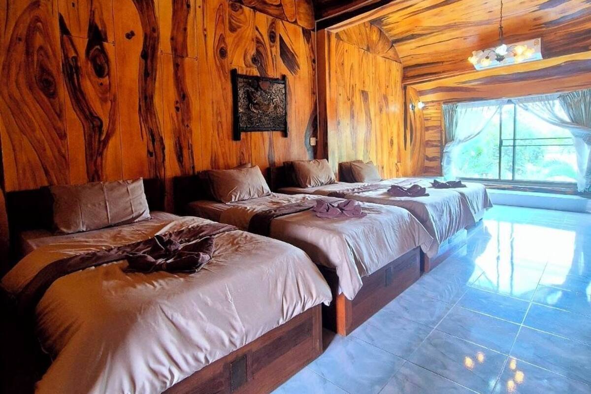 A wooden interior with a row of beds, a stone wall, and a large window.