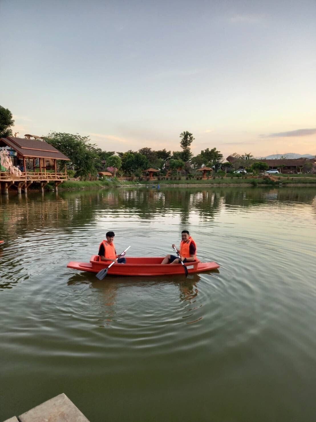 Dos personas en un canoa roja sobre aguas tranquilas, rodeado de árboles y edificios.