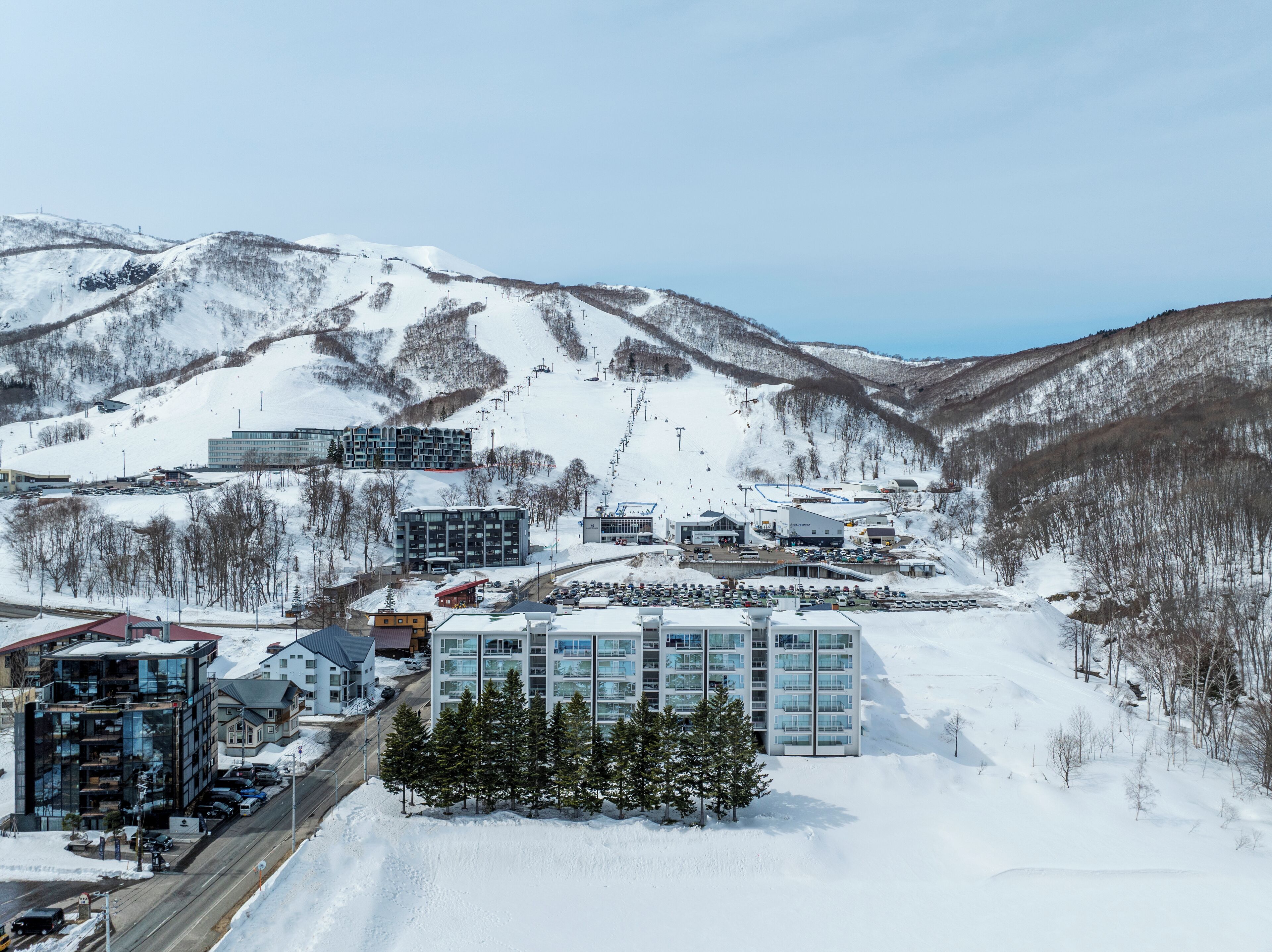 A modern hotel with a glass facade, located in a snowy mountainous area with ski slopes in the background.