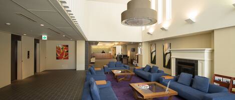 A lobby with sofas, coffee tables, a fireplace, and a staircase.