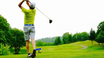 A golfer in a bright yellow shirt and gray shorts on a golf course with a clear sky and lush greenery.