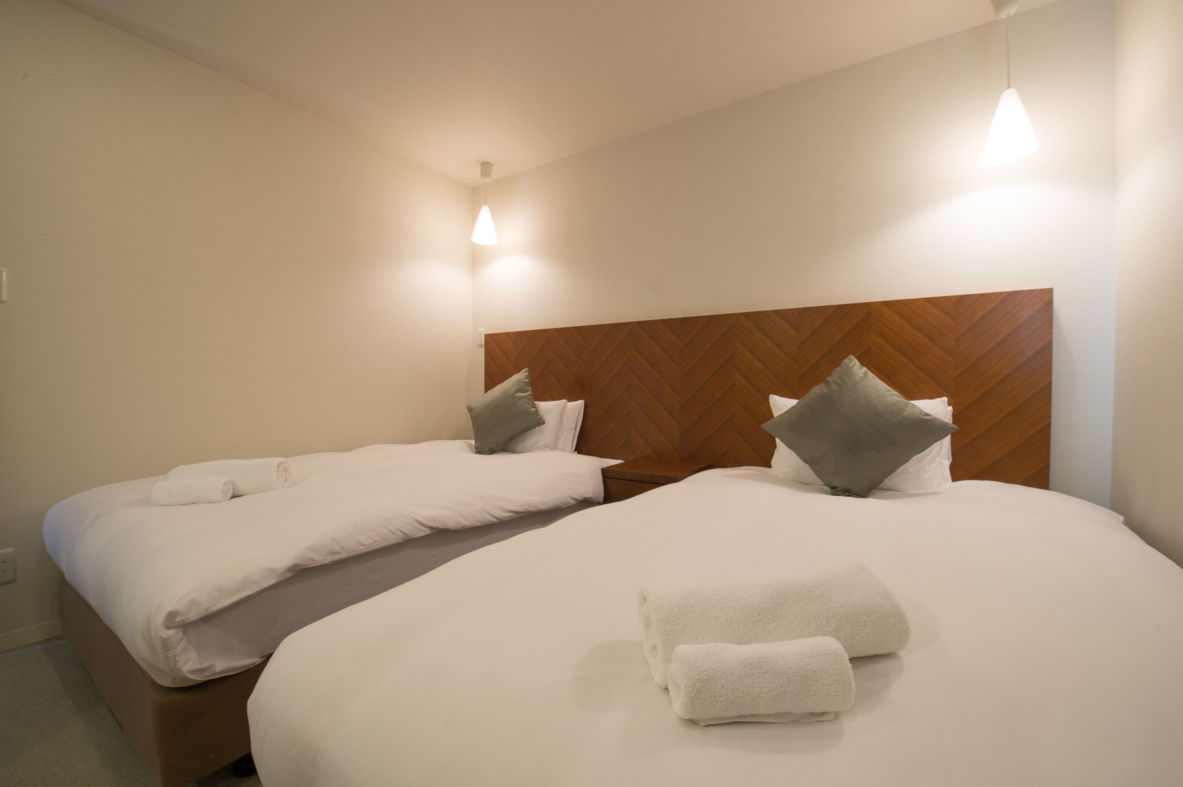 A hotel room with two beds, wooden headboards, white bedding, and two bedside lamps.