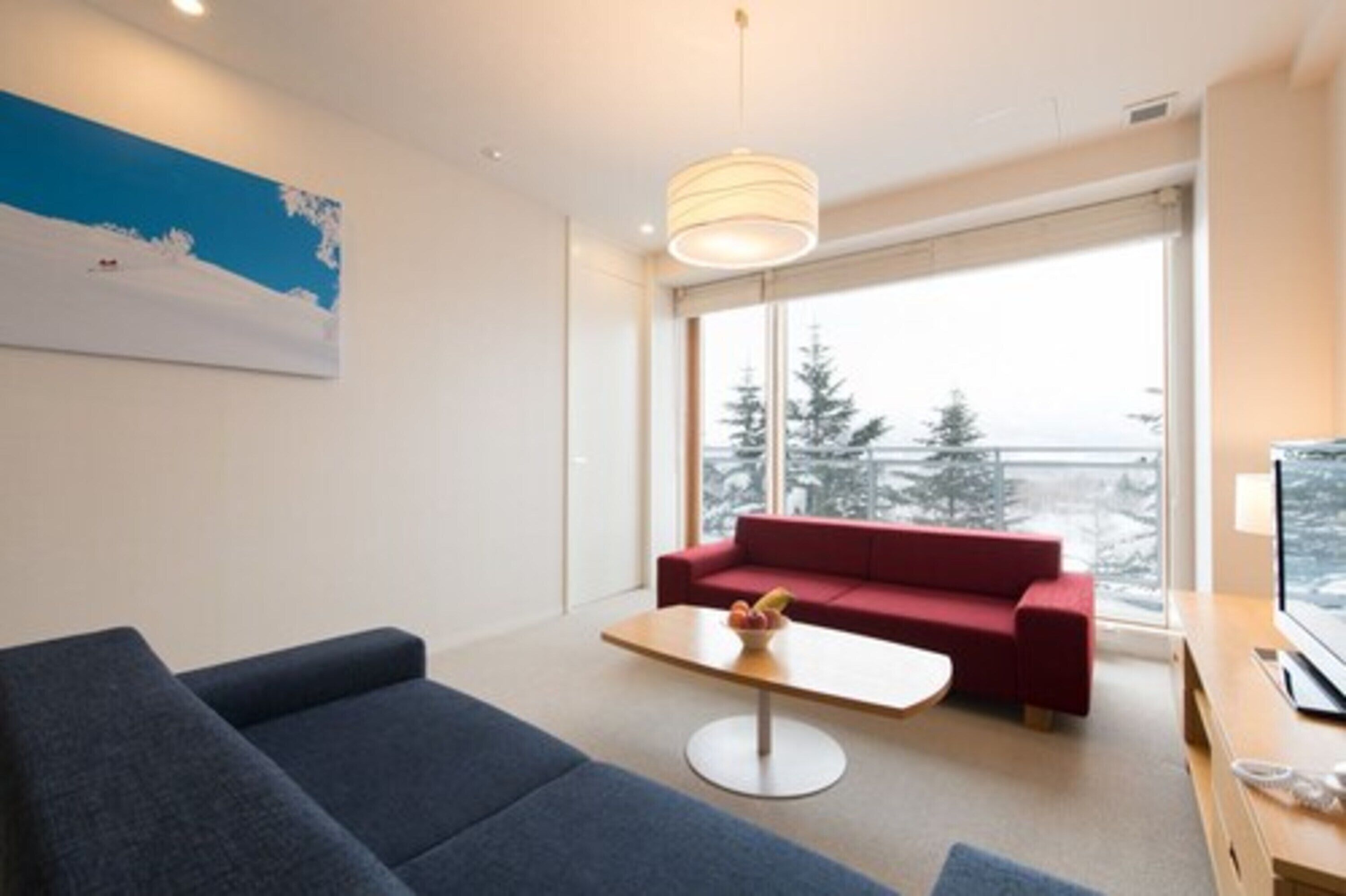 A modern living room with a red sofa, a blue couch, a small table with fruit, and a TV on a wooden stand.