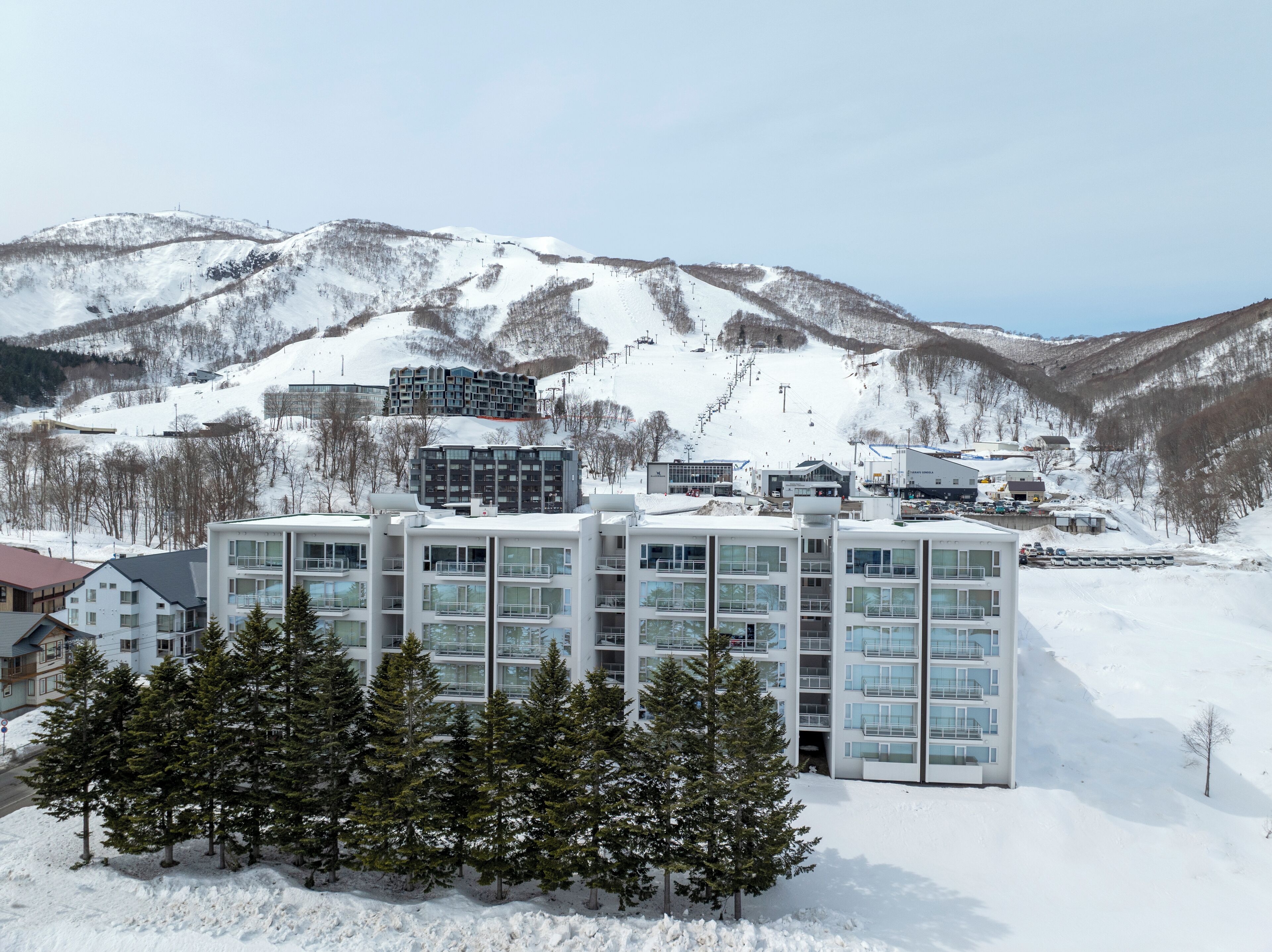 Een modern hotel met meerdere verdiepingen, grote ramen en uitzicht op een besneeerd berglandschap.