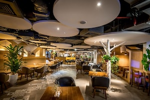 Restaurante moderno com tetos altos, iluminação pendente e diversos tipos de assentos.