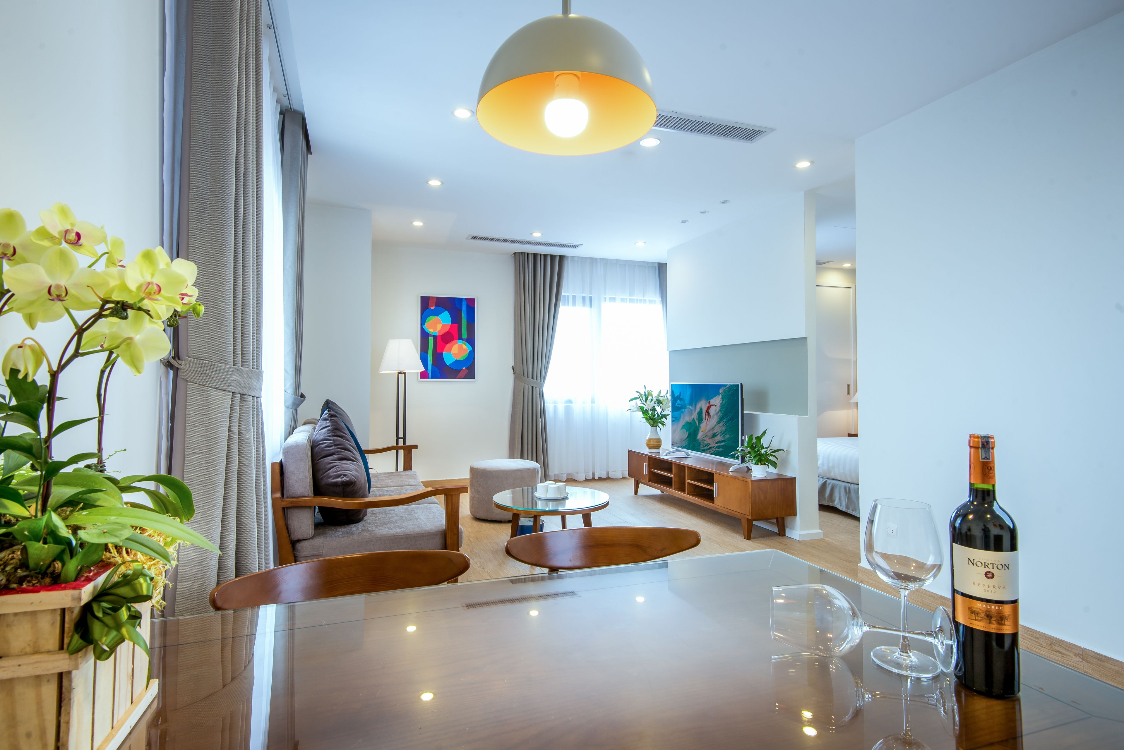 A modern living room with a wooden dining table, a sofa, a TV, and a plant.