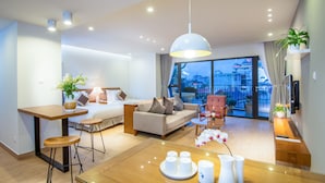 A modern hotel room with a large window, a dining area, a sofa, and a desk. - Dream Hotel & Apartment (Hanoi)