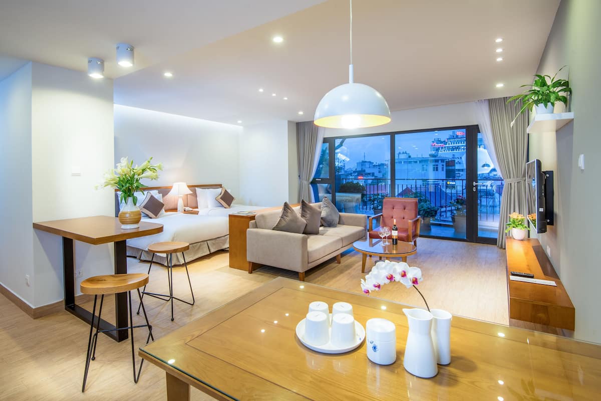 A modern hotel room with a large window, a dining area, a sofa, and a desk.