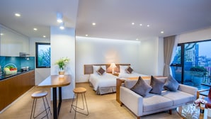A modern hotel room with a kitchen area, a sofa, a dining table, and a large window with a city view. - Dream Hotel & Apartment (Hanoi)