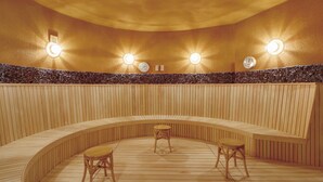 A sauna with wooden benches and tables, a stone wall, and wall-mounted lights. - Quad Inn Yokote (Yokote)