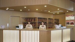 A reception desk with two staff members, a bulletin board with information, and a wall of hanging garments. - Quad Inn Yokote (Yokote)
