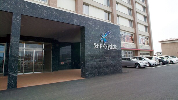 A building with a large glass entrance and a logo on the facade. - Quad Inn Yokote (Yokote)