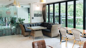 A modern lounge area with wicker furniture, a glass wall, and a cityscape view. - R1 Nimman Hotel Chiangmai (Chiang Mai)