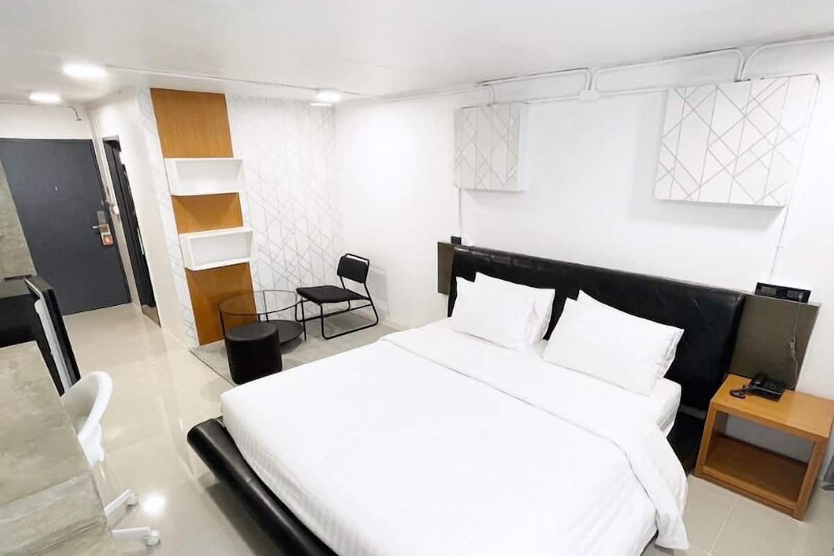 A modern hotel room with a large bed, a desk, a chair, and a small table.