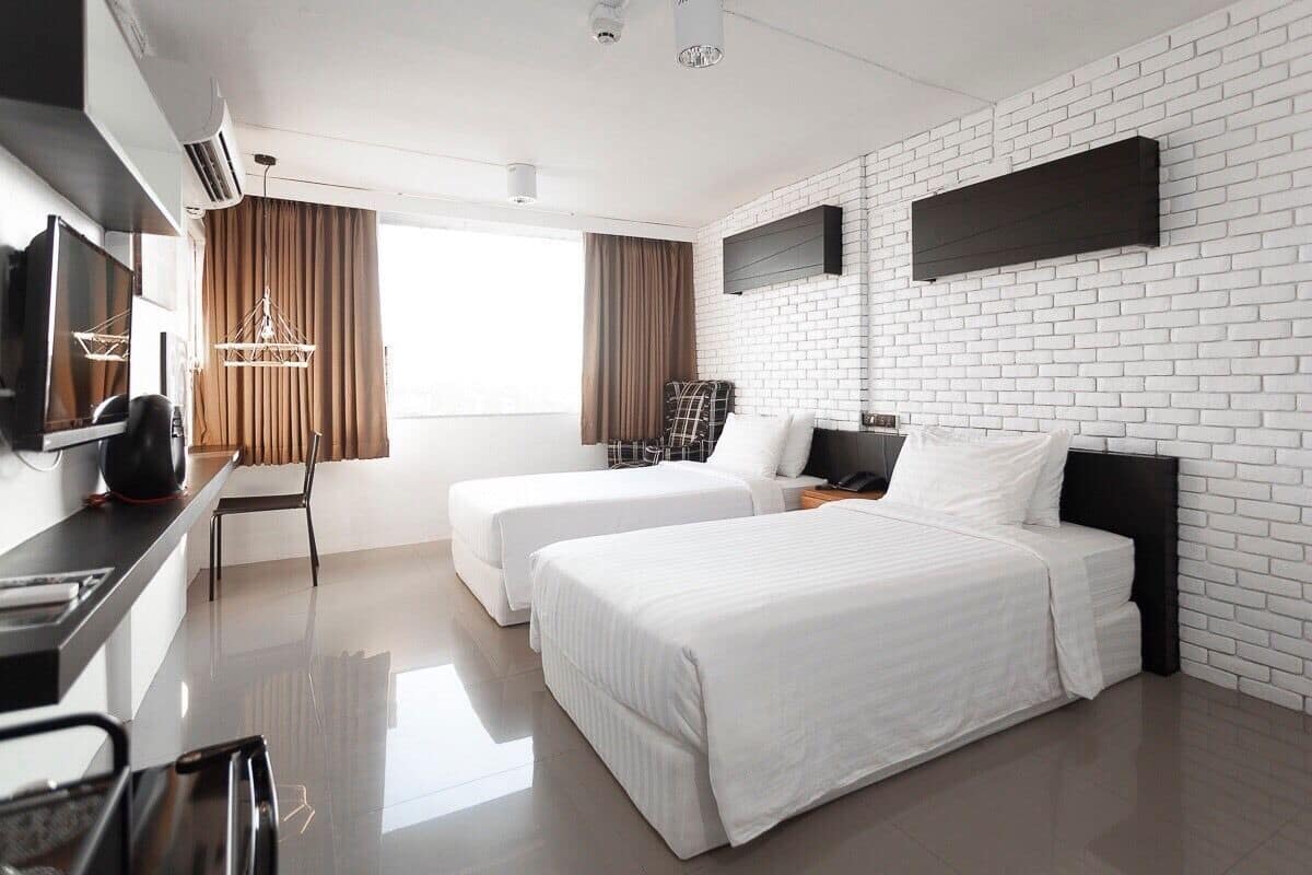A modern hotel room with two beds, a flat-screen TV, a desk with a chair, and a large window with curtains.