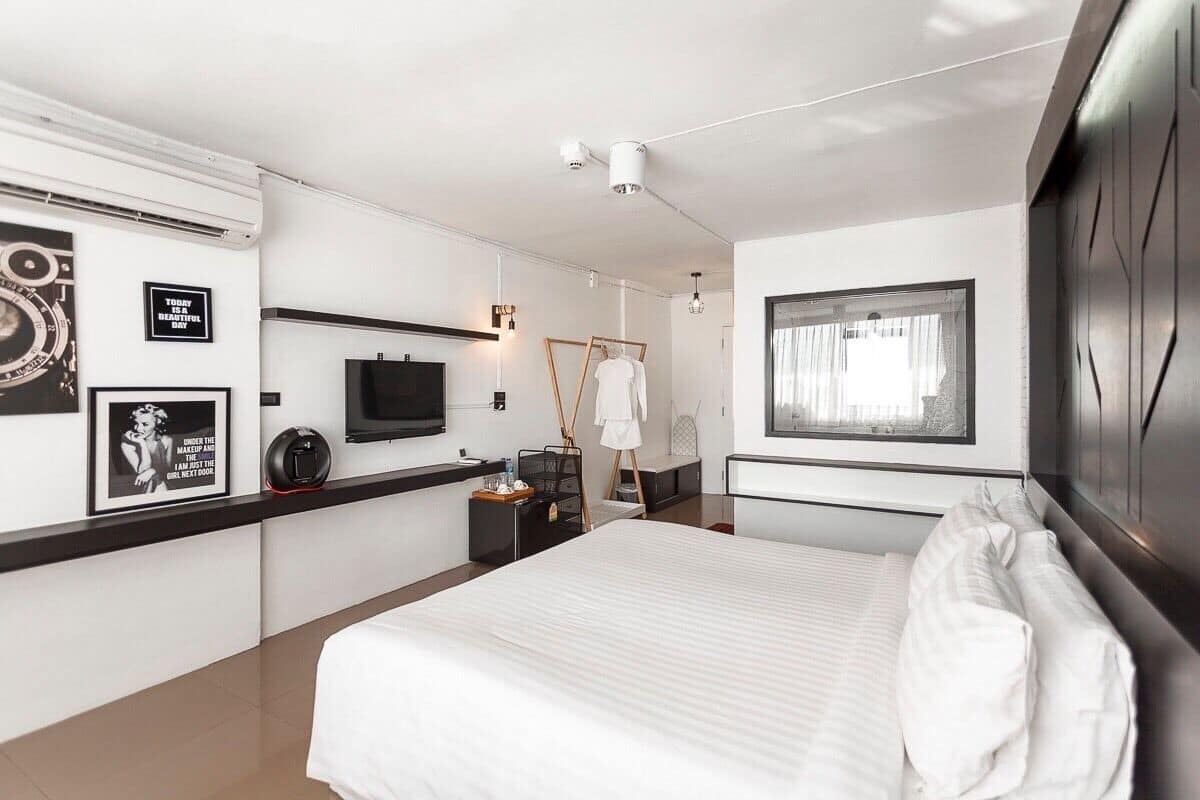 A modern hotel room with a large bed, a flat-screen TV, a wardrobe, and a window with curtains.