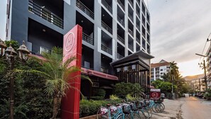 A hotel entrance with a red sign, a row of bicycles, and a parking area. - R1 Nimman Hotel Chiangmai (Chiang Mai)