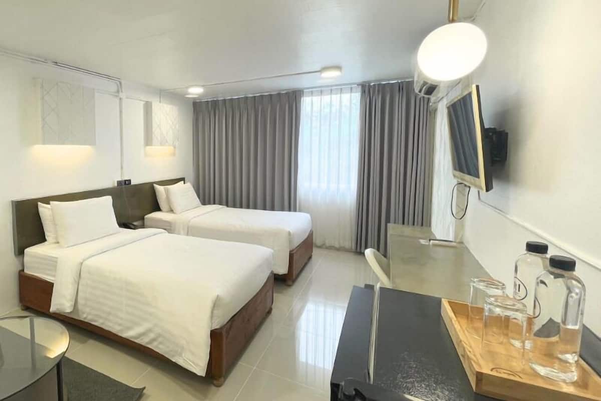 A hotel room with two beds, a desk, a chair, a TV, and a minibar.