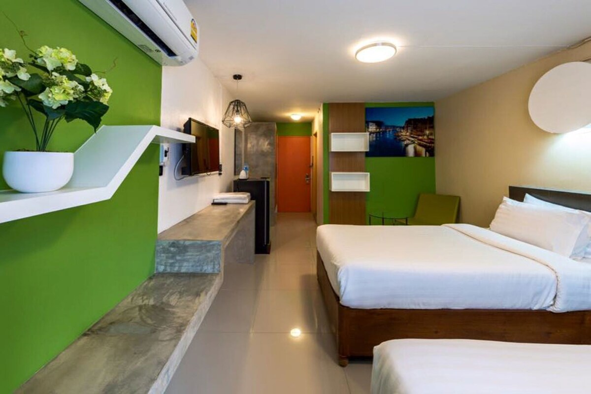A hotel room with a bed, a small desk, a chair, a TV, and a potted plant.
