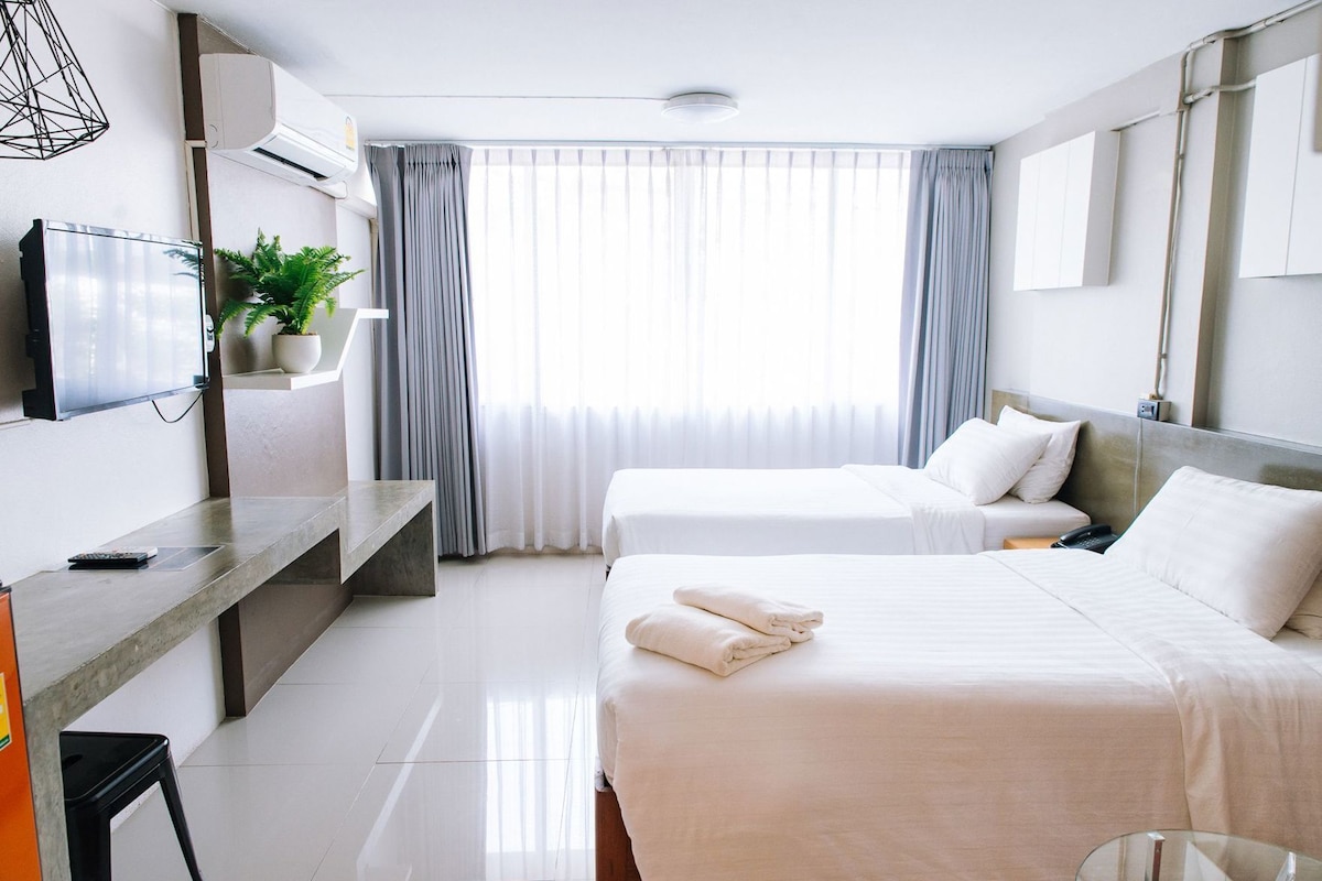 A hotel room with a bed, a desk, a TV, and a window with curtains.