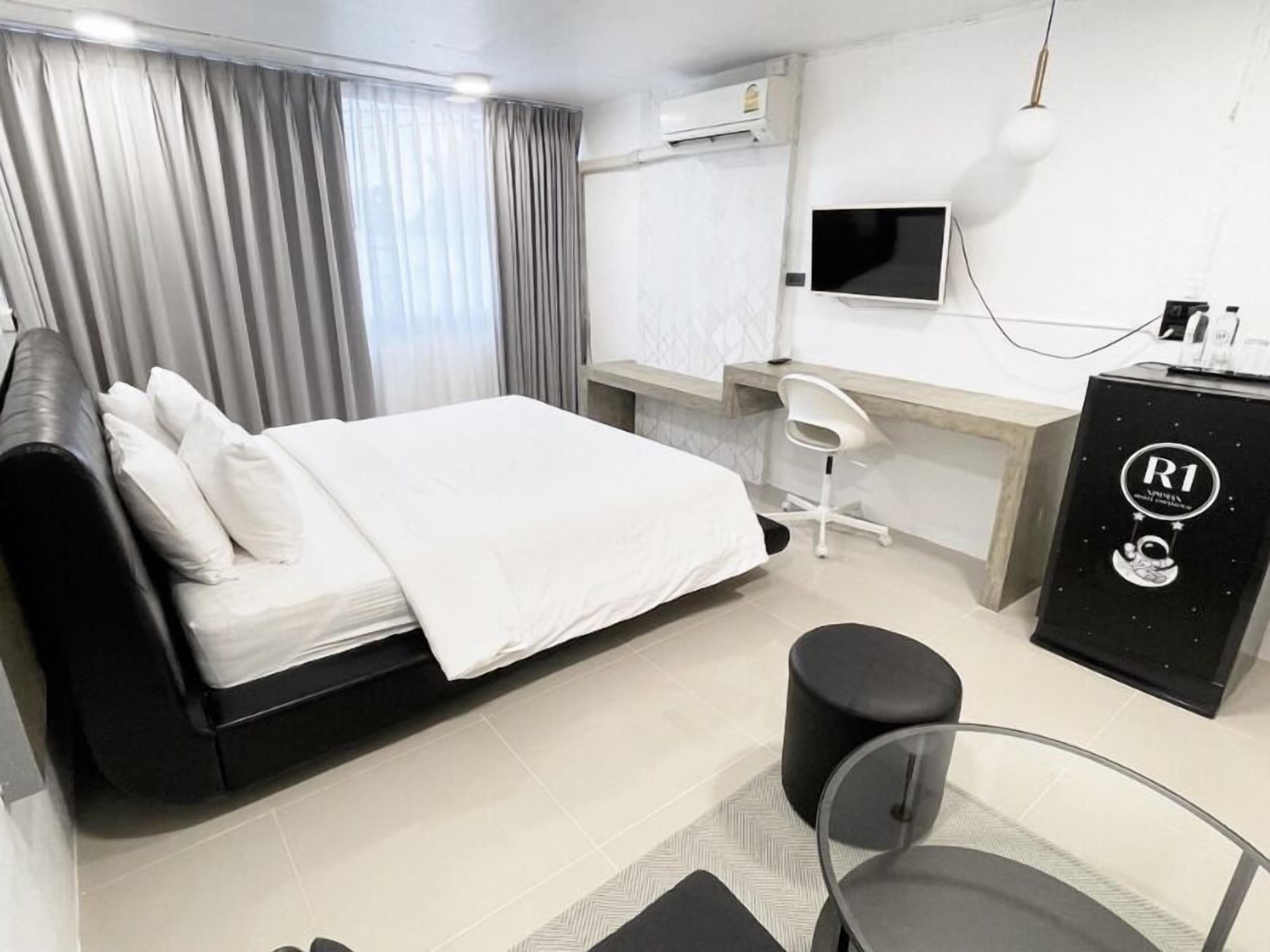 A modern hotel room with a bed, a desk, a chair, a TV, and an air conditioning unit.