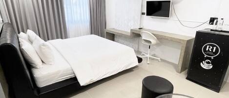 A modern hotel room with a bed, a desk, a chair, a TV, and an air conditioning unit.