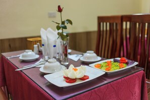 Una mesa de comedor dispuesta con vajilla blanca, un jarrón con una rosa y un plato de verduras en rodajas.