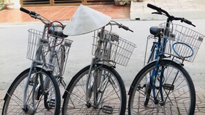 Tres bicicletas estacionadas sobre una superficie pavimentada con suelo de baldosas y una reja metálica al fondo.