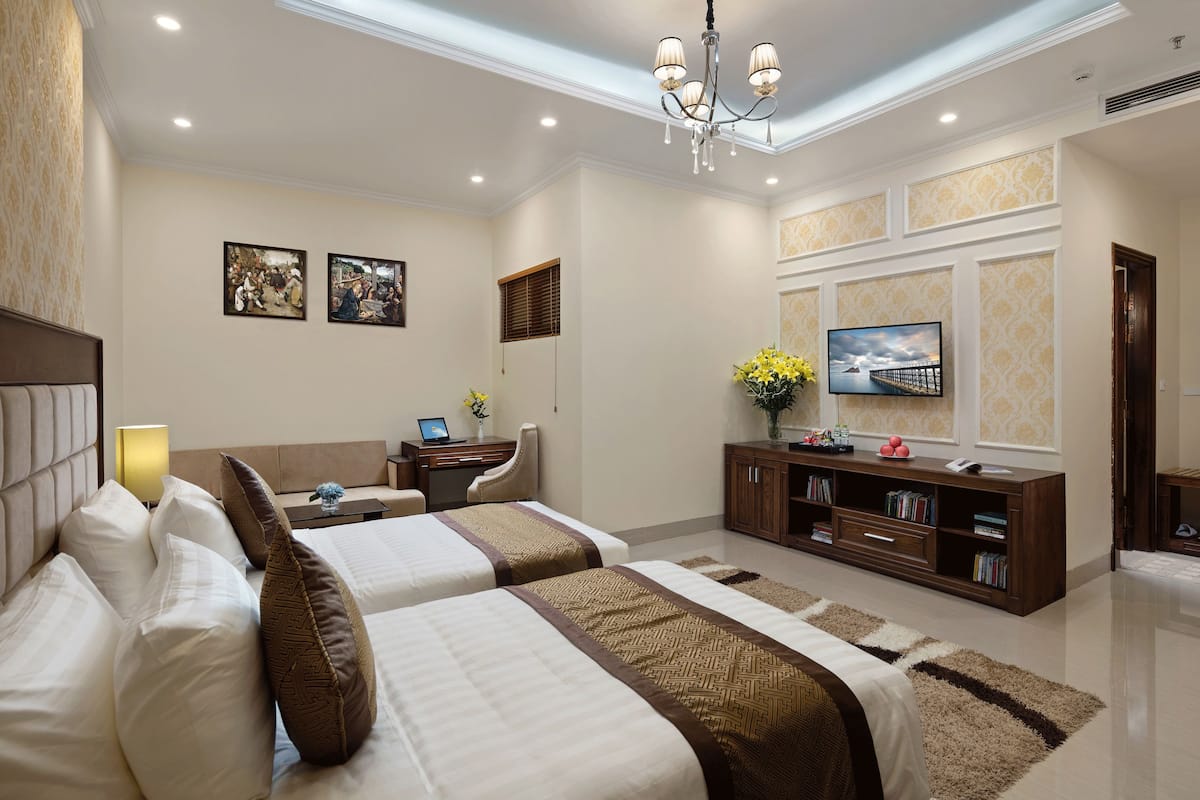 A hotel room with two beds, a desk, a television, and a bookshelf.
