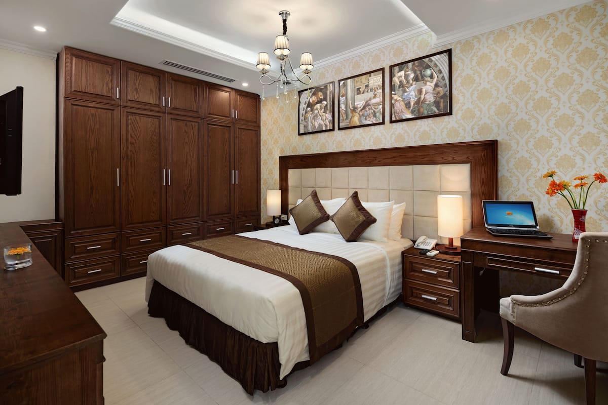 A bedroom with a large bed, wooden wardrobe, desk, and a laptop.