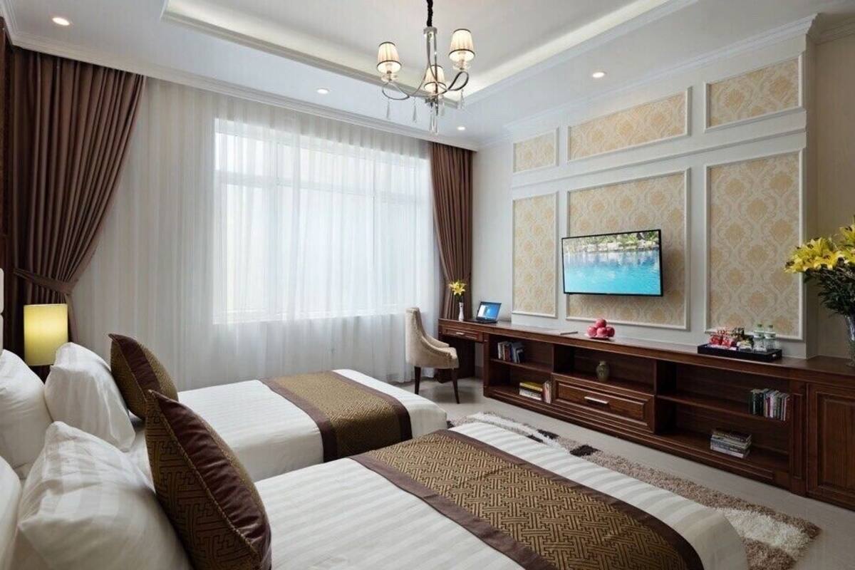 A hotel room with two beds, a desk, a TV, and a large window with curtains.