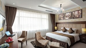 Habitación de hotel con una cama grande, un escritorio con una computadora portátil, una silla y una mesita con pasteles.