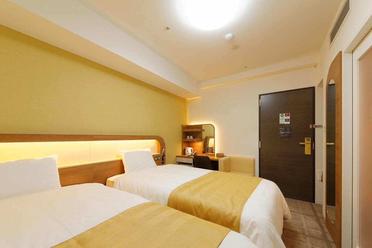 Ein Hotelzimmer mit zwei Betten, einem Schreibtisch, einem Stuhl und einer Tür.