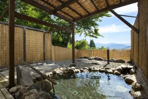 A traditional Japanese onsen with a wooden structure, a stone bath, and a view of mountains in the background. - Muica Onsen Hotel (Minamiuonuma)