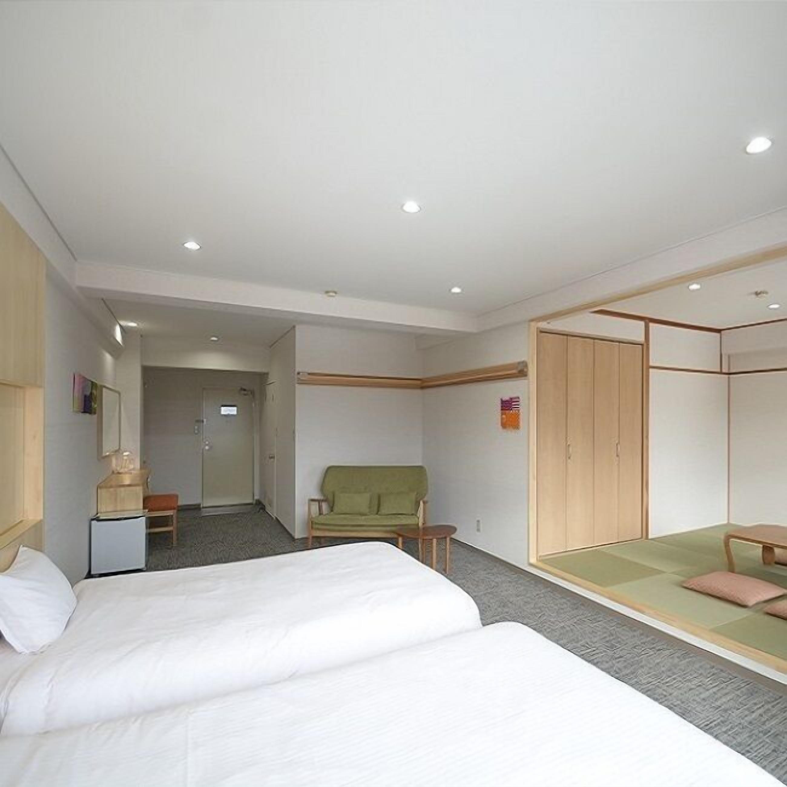 A hotel room with two beds, a green sofa, a wooden wardrobe, and a small table.