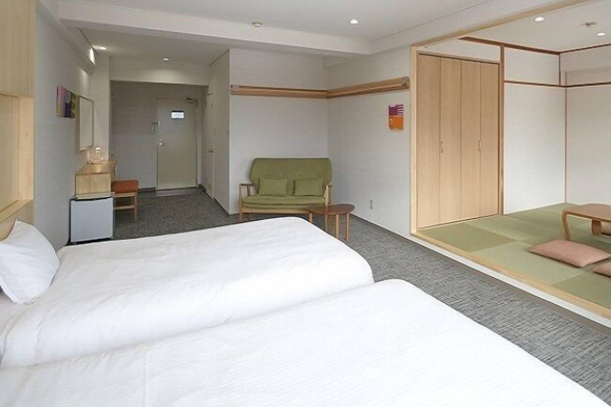 A hotel room with two beds, a green sofa, a wooden wardrobe, and a small table.
