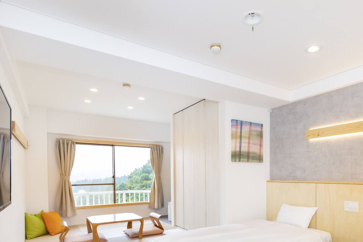 A hotel room with a bed, a sofa, a table, and a window with curtains.