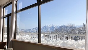 A room with a large window overlooking a snowy mountain landscape. - Muica Onsen Hotel (Minamiuonuma)