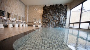 A modern indoor swimming pool with tiled flooring, multiple changing stations, and a stone wall. - Muica Onsen Hotel (Minamiuonuma)