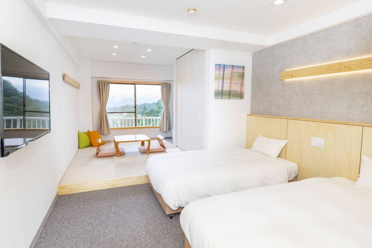 A modern hotel room with two beds, a large window with a view, a flat-screen TV, and a wooden headboard.