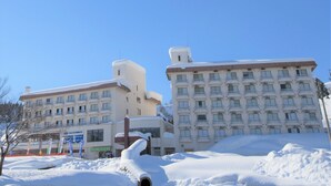 A hotel with multiple floors, balconies, and a snow-covered ground. - Muica Onsen Hotel (Minamiuonuma)