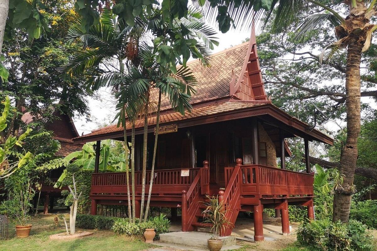 A traditional wooden structure with a tiled roof, surrounded by lush greenery and palm trees.