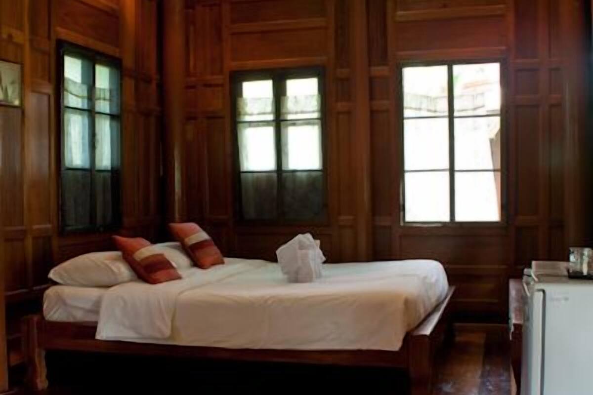 A wooden-paneled room with a bed, a small table, and a refrigerator.