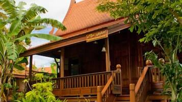 A wooden house with a tiled roof, surrounded by lush greenery and a stone pathway leading to the entrance.