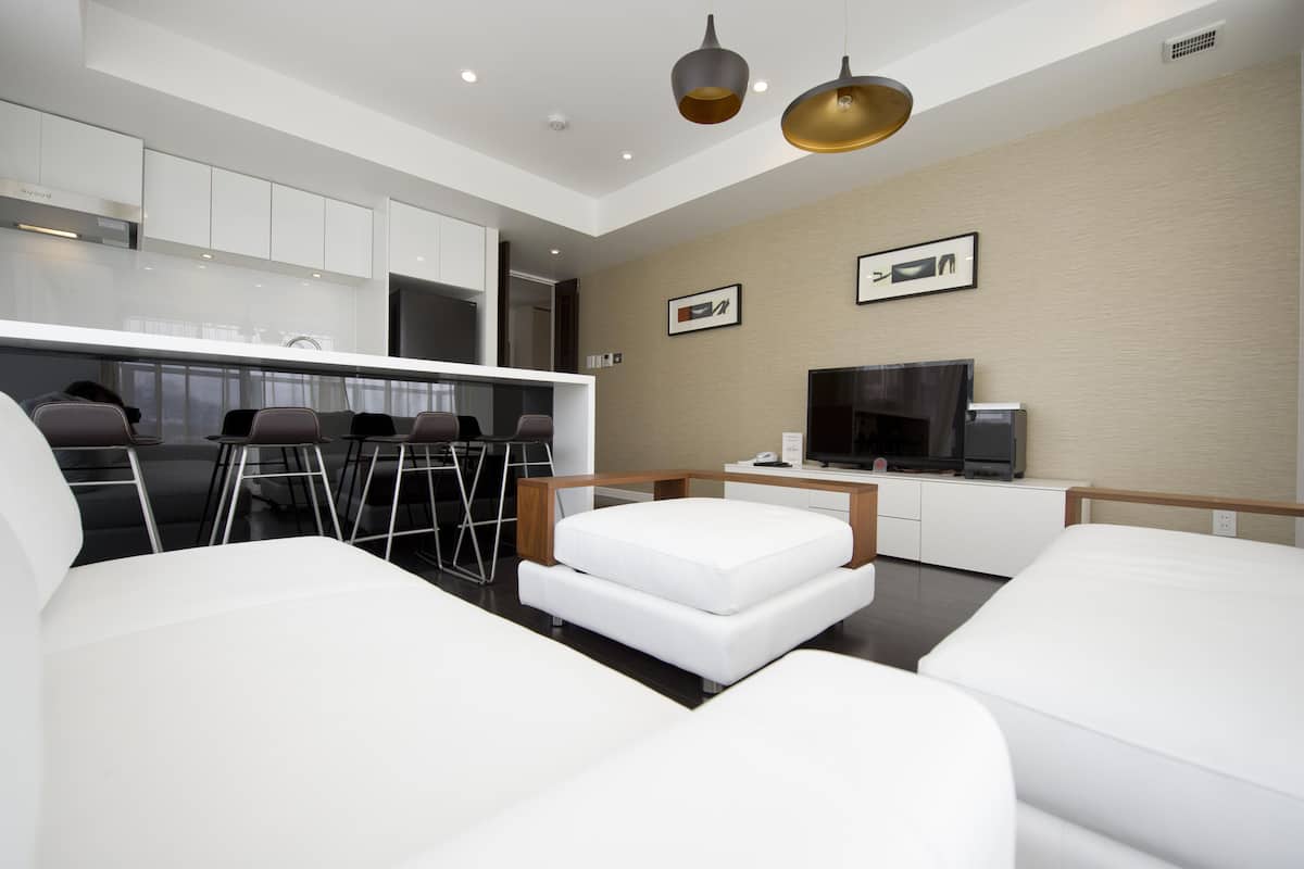 A modern living room with a sofa, a small white ottoman, and a TV.