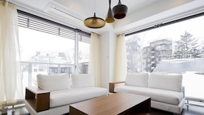 Una sala de estar moderna con un sofá blanco, una mesa de centro de madera y ventanas grandes con cortinas.