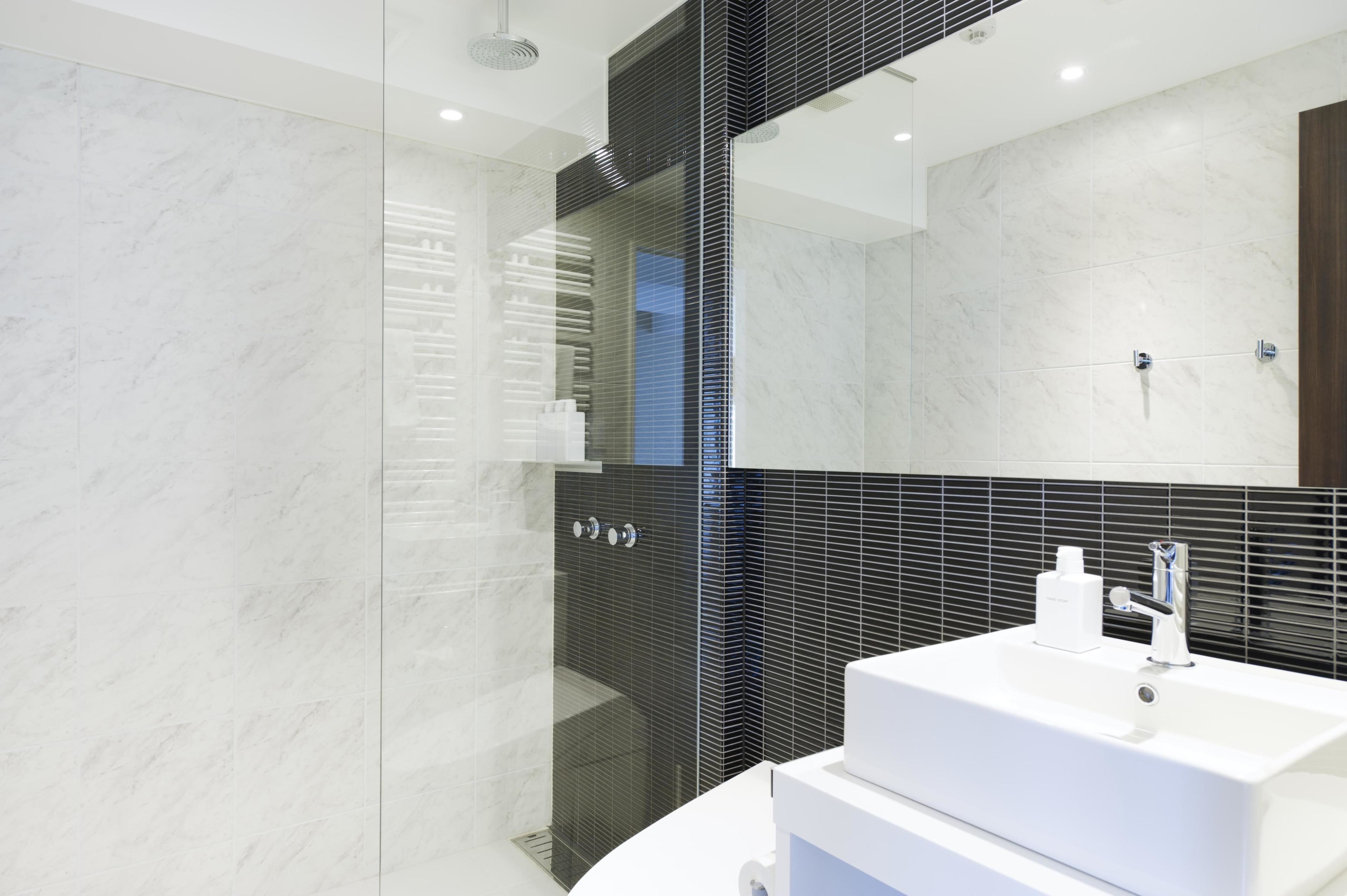A modern bathroom with a glass-enclosed shower, a white sink, and a large mirror.